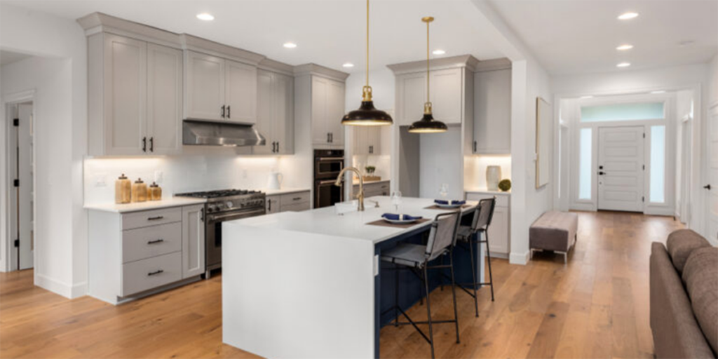A modern, newly remodeled kitchen featuring light gray cabinets, a large central island with barstools, and elegant pendant lighting.